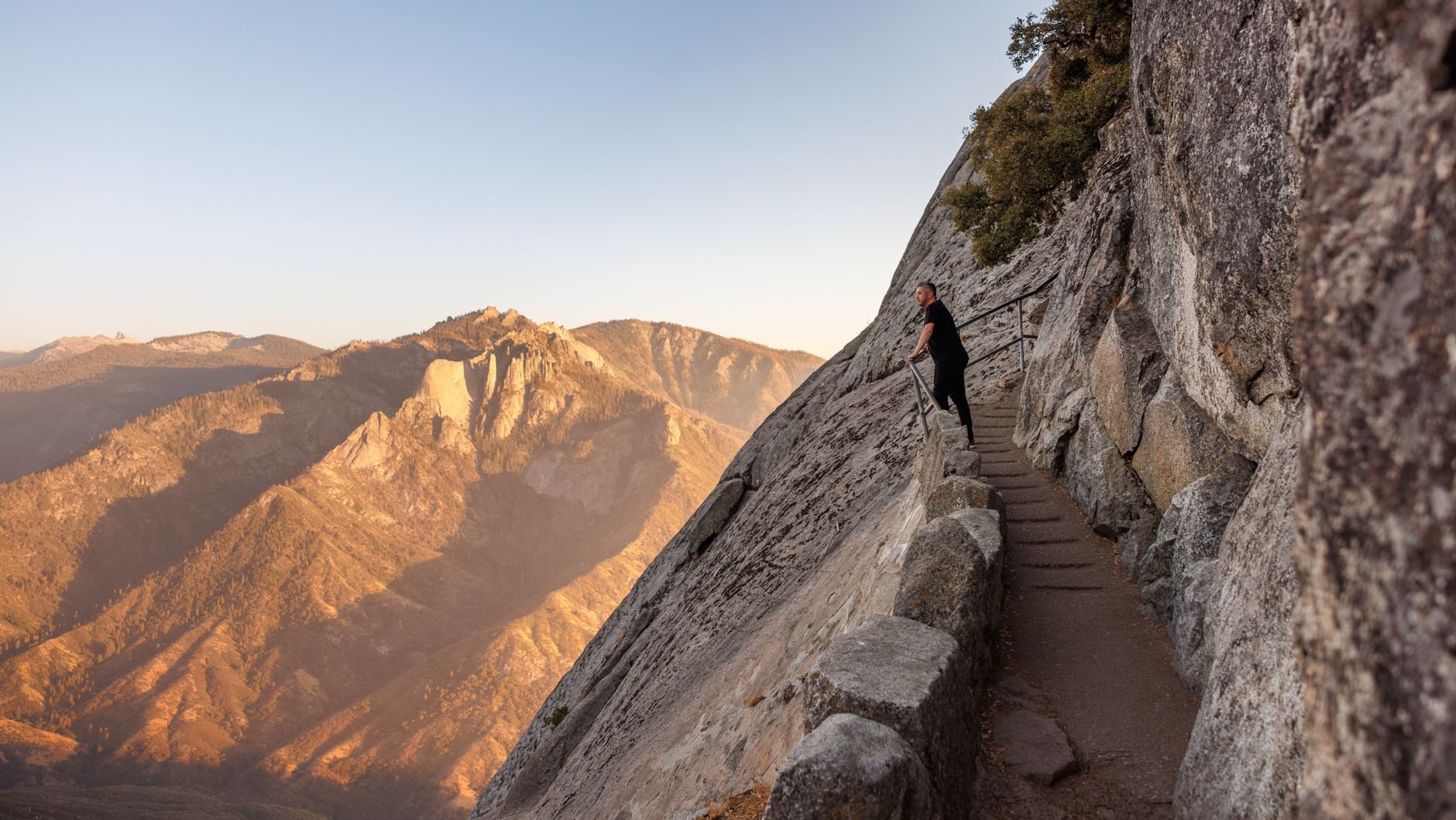 Hiker on a rocky mountain trail at sunset, overlooking sweeping high-country views